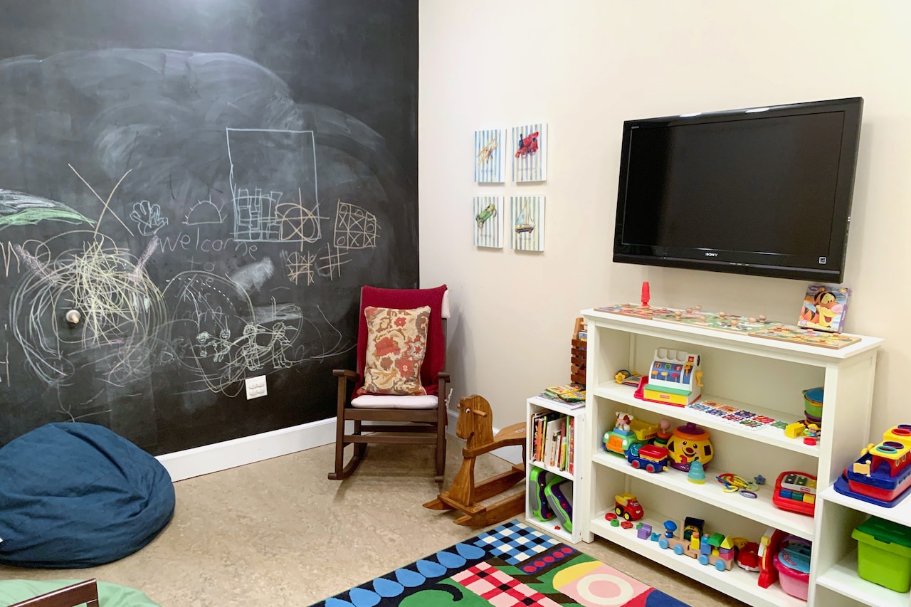 A children’s room has toys, a rocking chair, a beanbag chair, and a chalkboard wall covered in colorful scribbling.