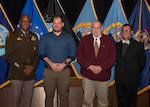 One Man in Army Uniform with three men in civilian dress