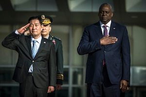 Women and men wearing suits and military uniforms pose for a photo.