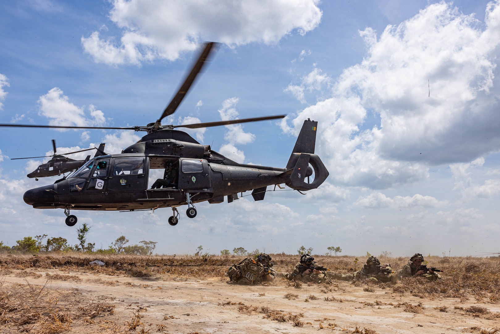 Soldiers are positioned on the ground as a helicopter takes off.