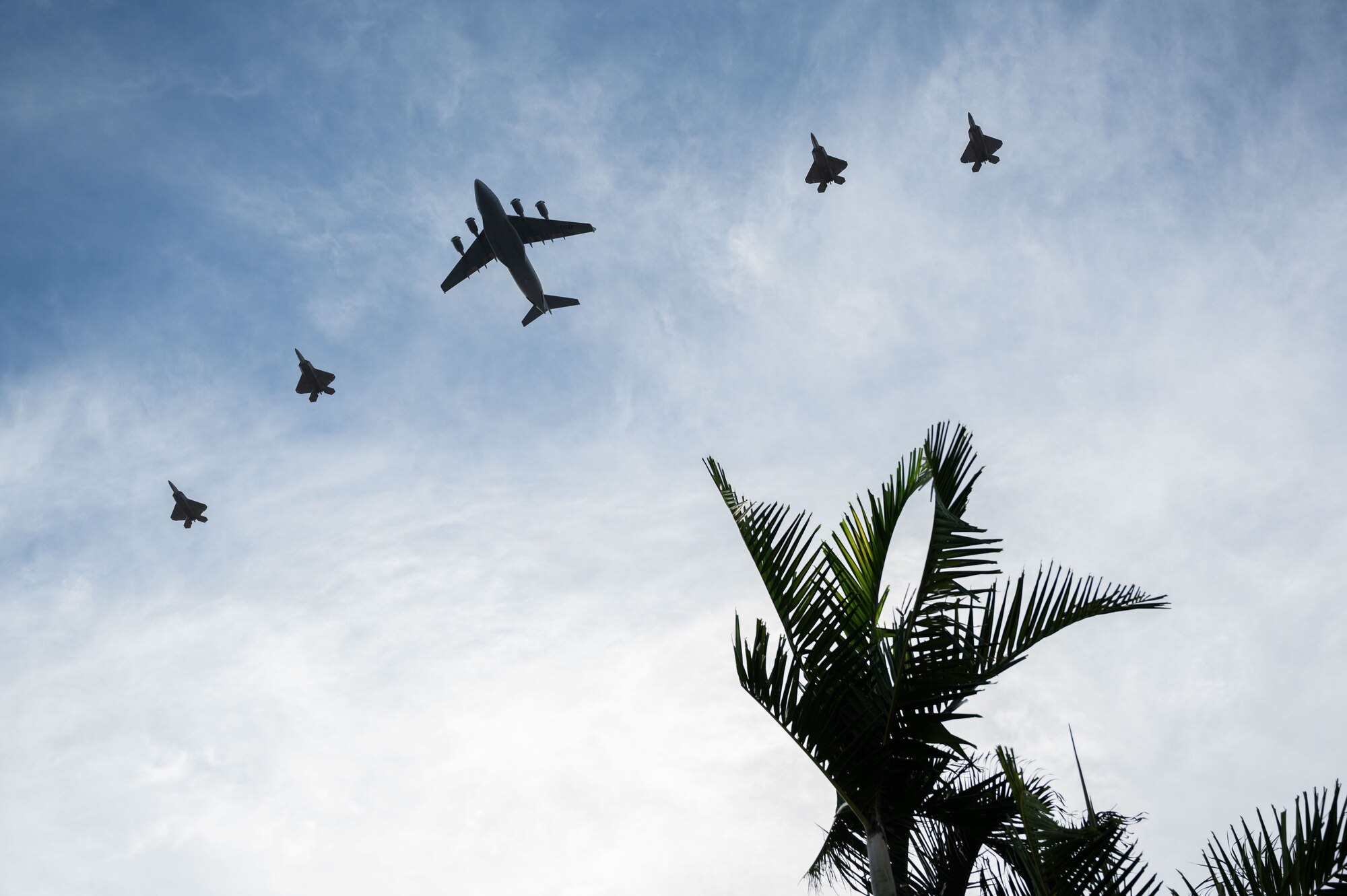 Four Hawaii Air National Guard F-22 Raptors and a C-17 Globemaster III from the 535th Airlift Squadron conduct a flyover of the opening ceremony for the Pacific Air Chiefs Symposium 2023 at Joint Base Pearl Harbor-Hickam, Hawaii, Nov. 14, 2023. Air Chiefs from more than 20 countries participated in PACS 23 which aims to strengthen alliances and partnerships throughout the region. (U.S. Air Force photo by Tech. Sgt. Hailey Haux)