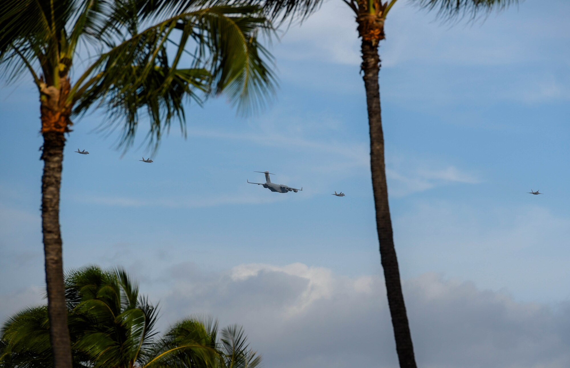 Four Hawaii Air National Guard F-22 Raptors and a C-17 Globemaster III from the 535th Airlift Squadron conduct a flyover of the opening ceremony for the Pacific Air Chiefs Symposium 2023 at Joint Base Pearl Harbor-Hickam, Hawaii, Nov. 14, 2023. This year’s symposium, the largest in history, focused on applying global lessons to the challenges of regional security. (U.S. Air Force photo by Airman 1st Class Caroline Strickland)