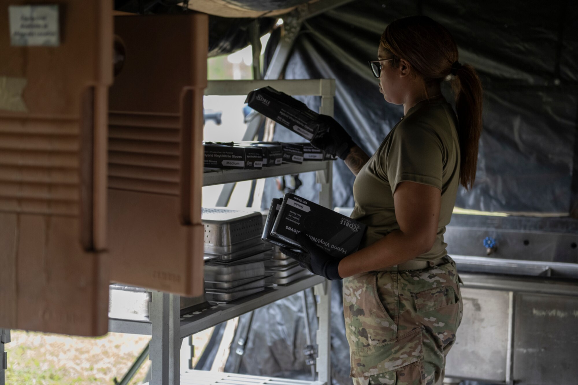 U.S. Air Force Staff Sgt. Ross Darlyn Rivera-Hernandez, 23rd Force Support Squadron team lead, stacks gloves on a shelf during exercise Mosaic Tiger 24-1 at Avon Park Air Force Range, Florida, Nov. 14, 2023. Rivera-Hernandez and her team stocked the kitchen in preparation of feeding personnel hot meals in the contingency location. (U.S. Air Force photo by Senior Airman Rachel Coates)