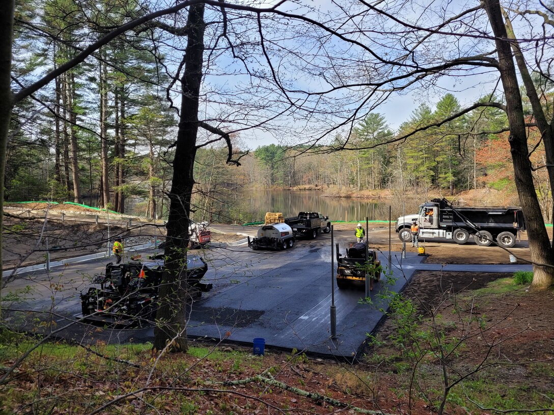 Heavy machinery pave asphalt in a wooded setting