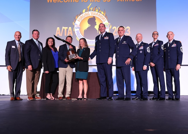 A group of award recipients stand on stage and pose for a photo with their trophy