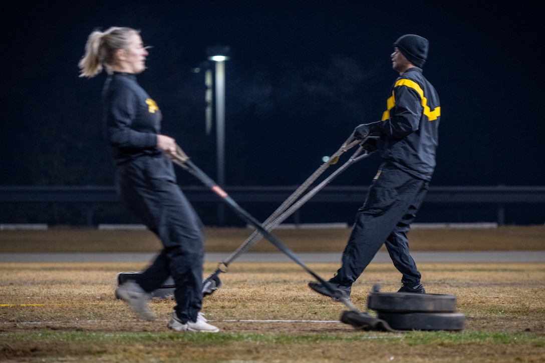 Cadets pull ropes to move weights across a field in the early morning hours.