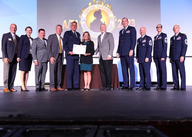 A group of award recipients pose on stage for a photo with their trophy