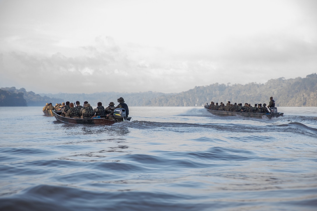Three rafts carrying service members sail in open water on a cloudy day.
