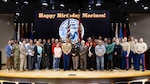 Large group of people stand on stage with a Happy Birthday Marine's in the background.