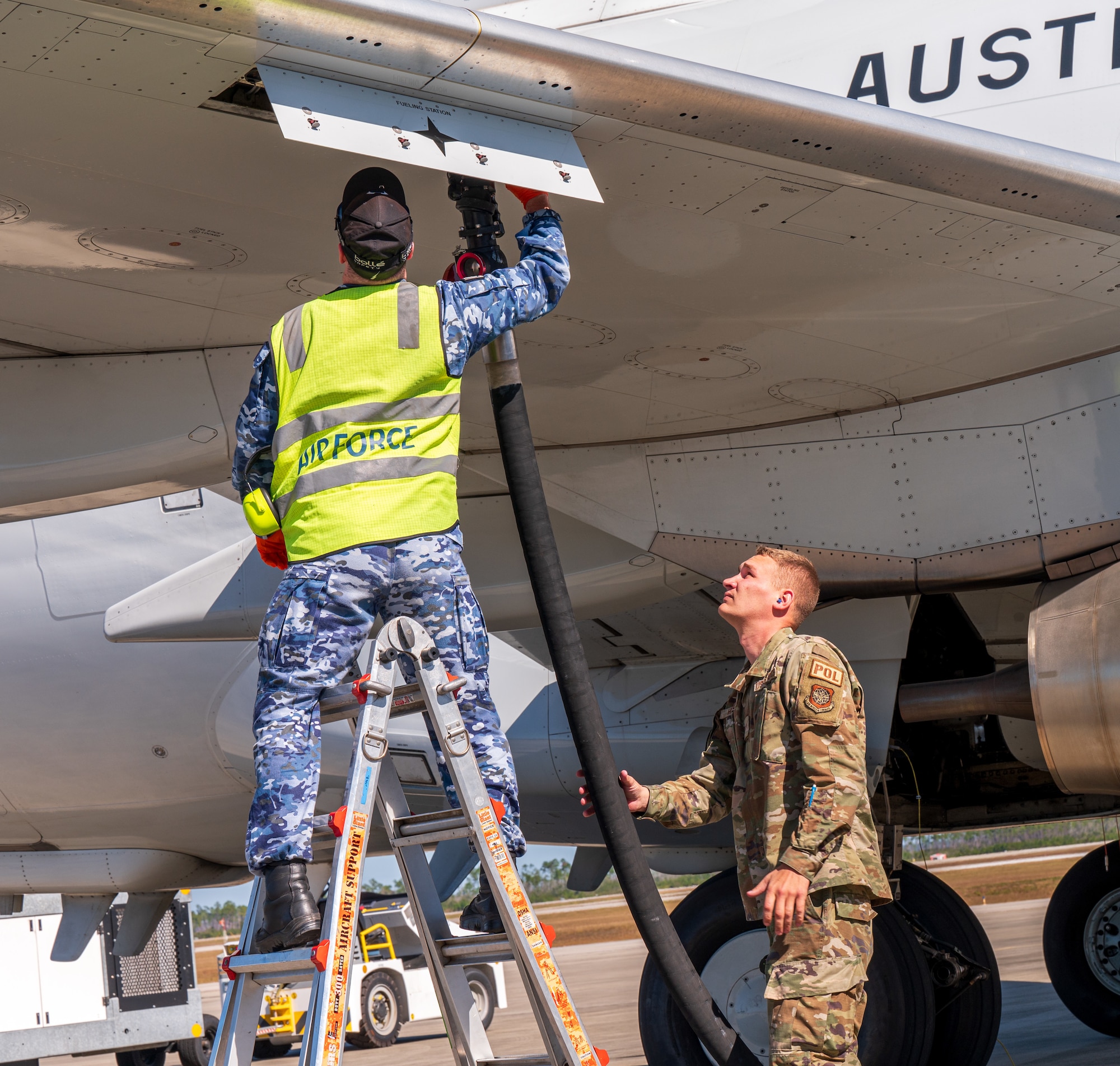 An Airman assists a Royal Australian Air Force aircraftman with refueling