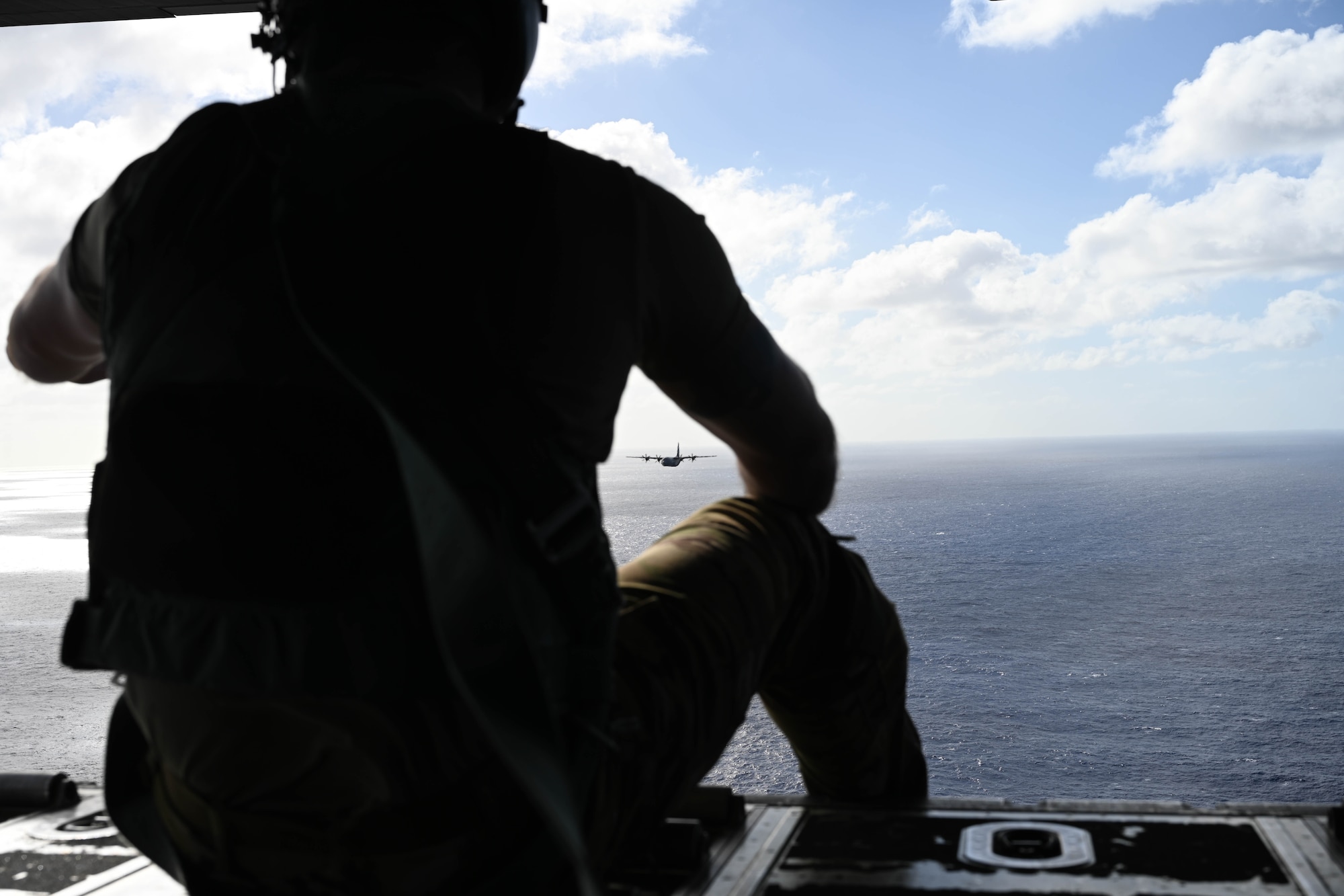 A man in uniform watches a military aircraft fly over the ocean