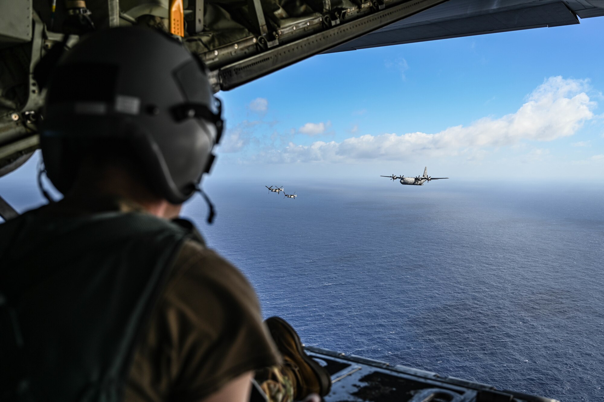 A man in uniform wearing a helmet watches military aircraft fly over the ocean