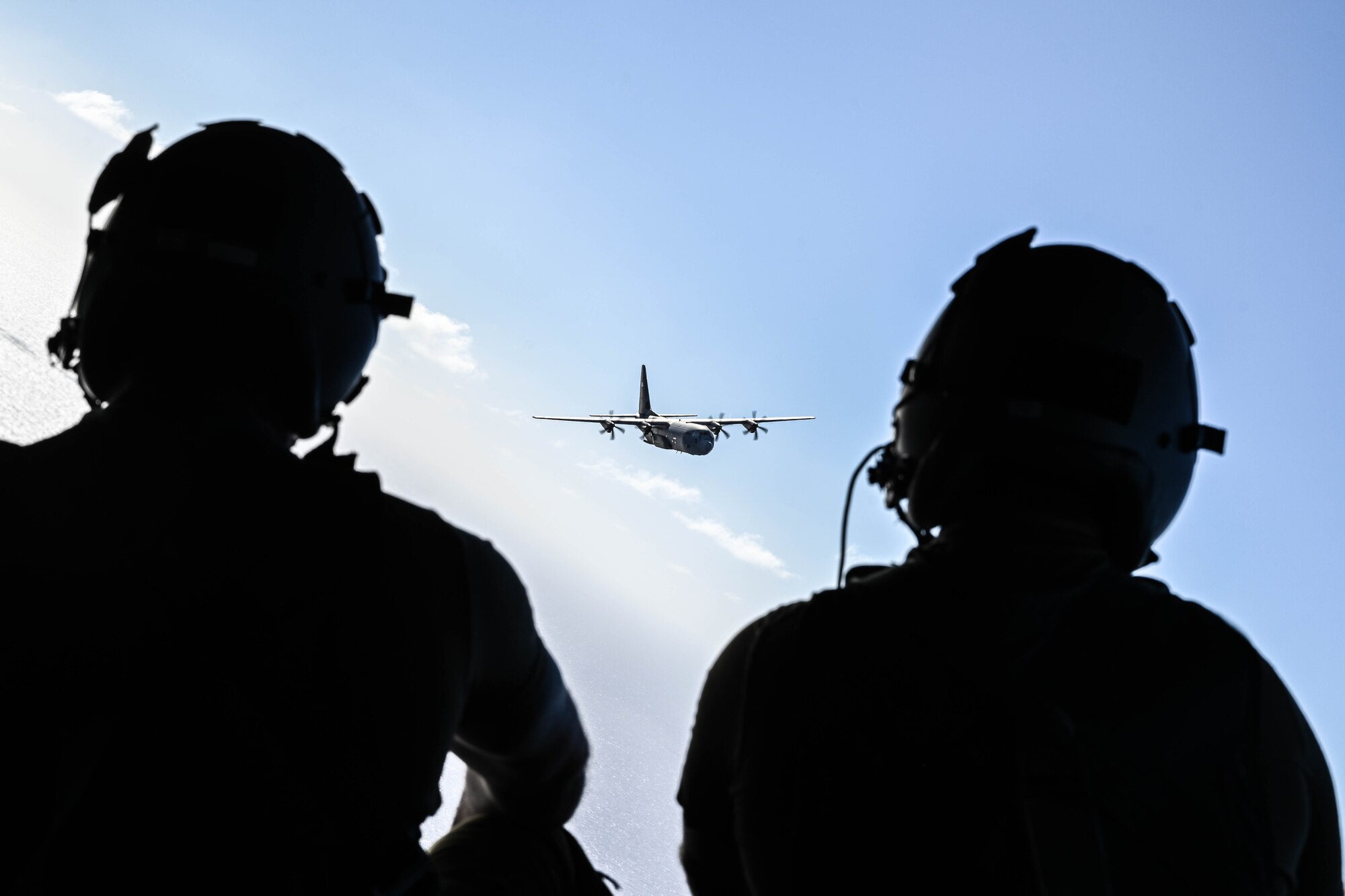Two people wearing helmets watch a military aircraft
