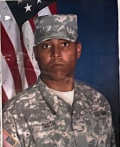Man wearing U.S. Army uniform posing in front of U.S. Flag