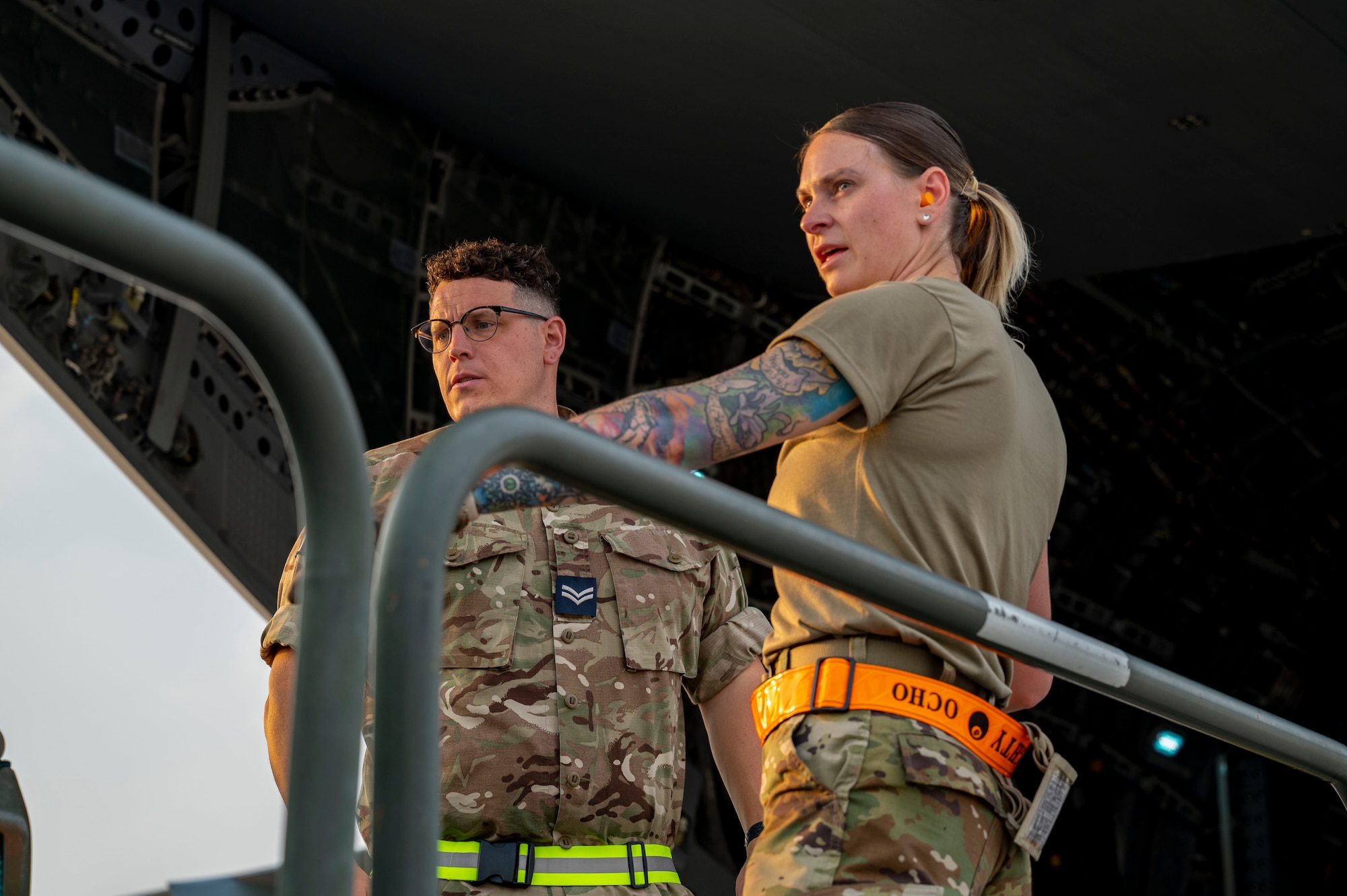 A U.S. Air Force Airman and a Royal Air Force logistics mover discuss plans for unloading cargo from the back of an RAF A400M Atlas.