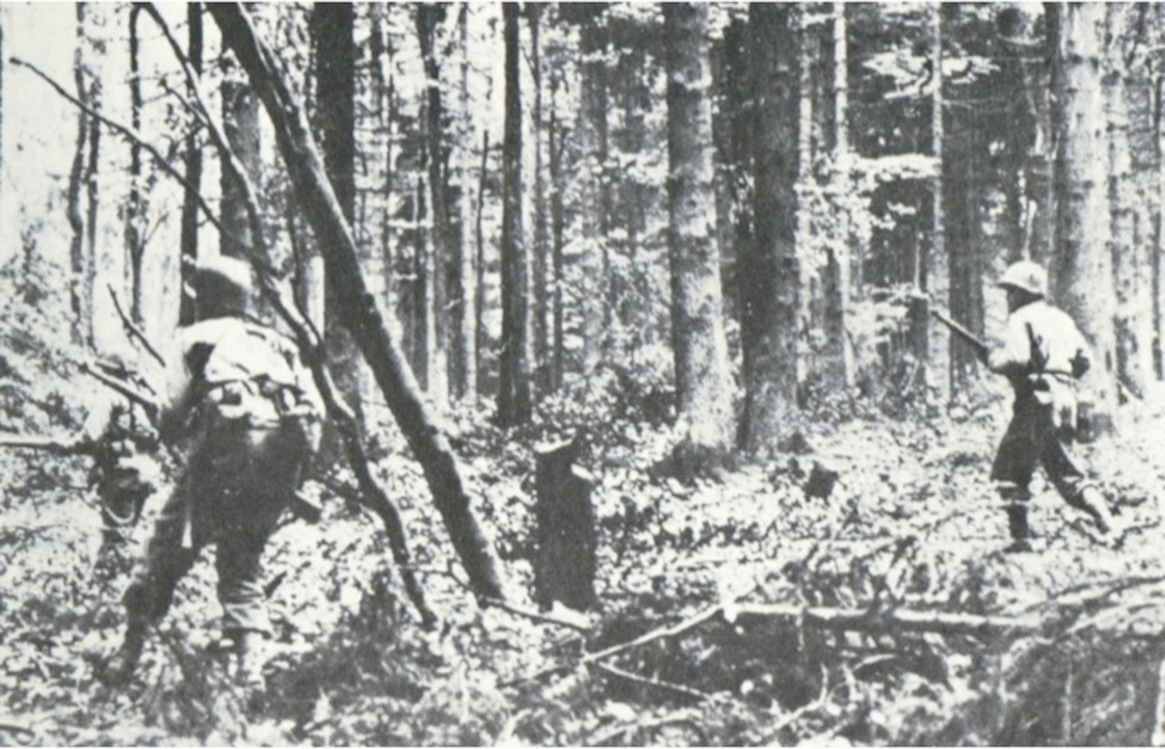 Two men with rifles move through a forest.