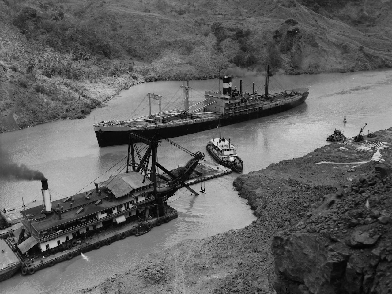 A ship moves through a narrow waterway as another dredging ship attempts to widen the lane.