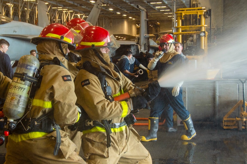 Sailors use a fire hose during training.