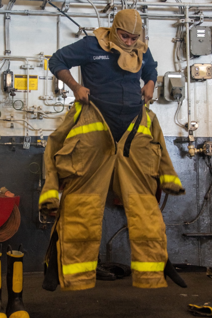 A sailor puts on a firefighting uniform.