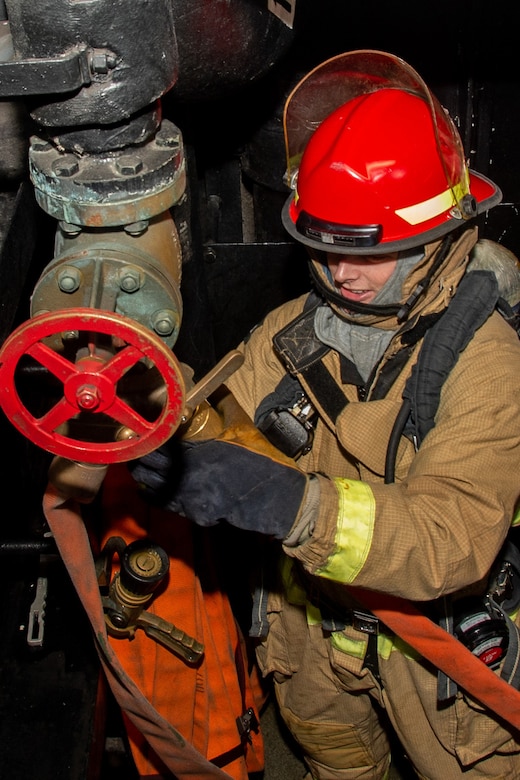 A sailor attaches a fire hose to a fire main plug.