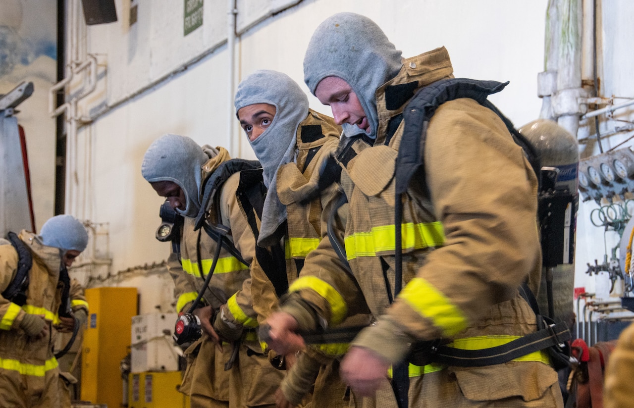Three sailors put on firefighting uniforms.