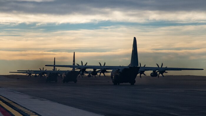 Three C-130 aircraft in a row taxi away from the camera.
