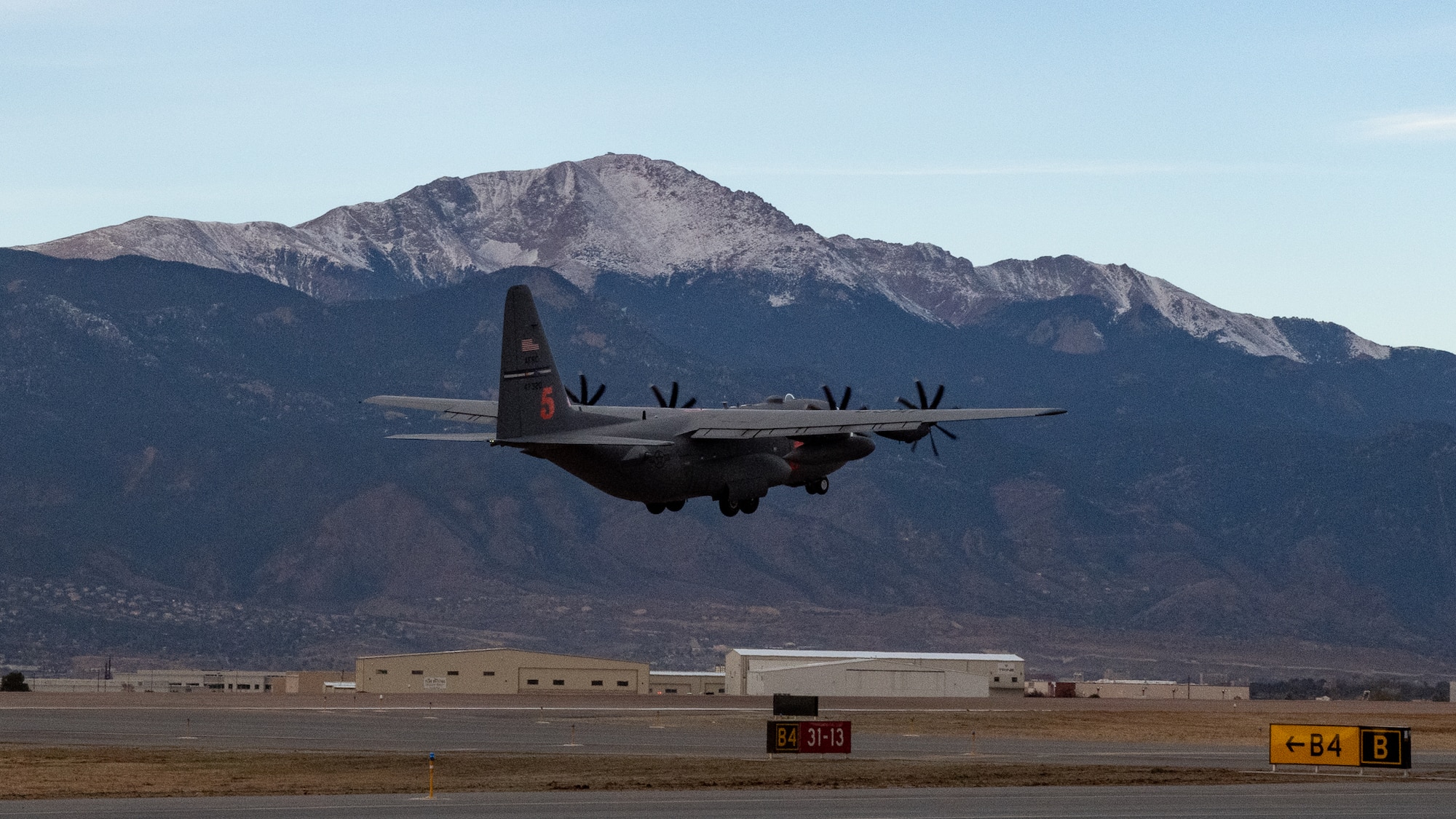 A C-130 takes off from a runway with Pikes Peak in the background.