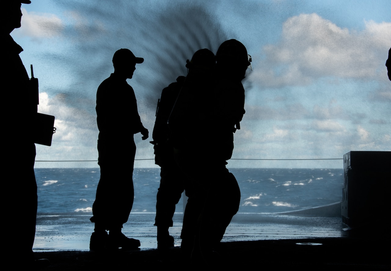 A silhouette of sailors engaging in a simulated fire.
