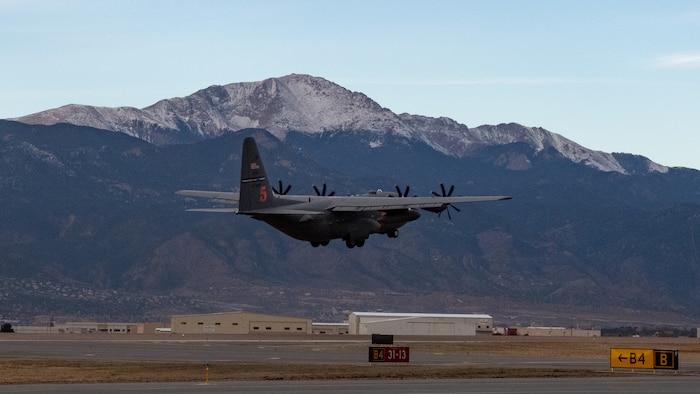 A C-130 takes off from a runway with Pikes Peak in the background.