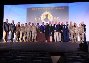 A group of award recipients pose on stage for a photo with their trophy