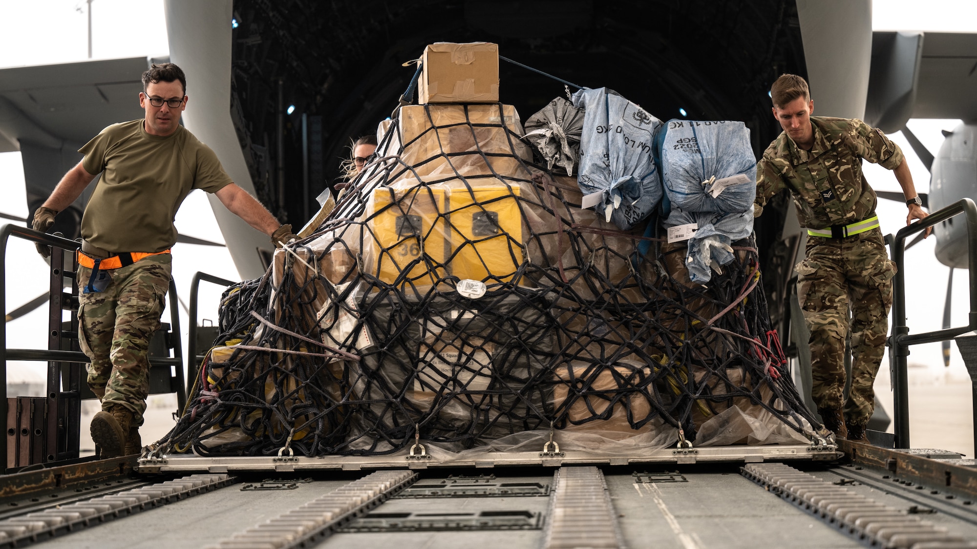 A U.S. Air Force Airman and Royal Air Force aviator unload cargo from a RAF A400 Atlas.