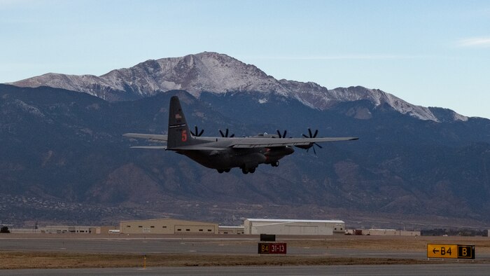 A C-130 takes off from a runway with Pikes Peak in the background.