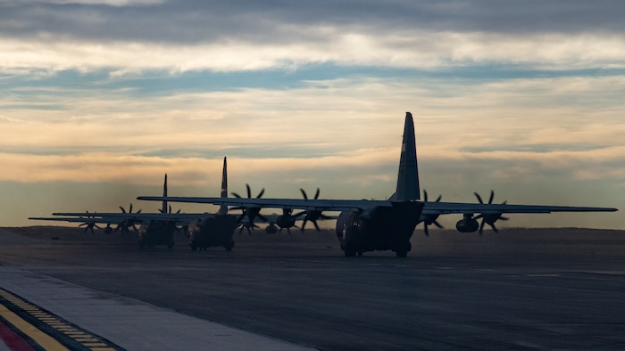 Three C-130 aircraft in a row taxi away from the camera.