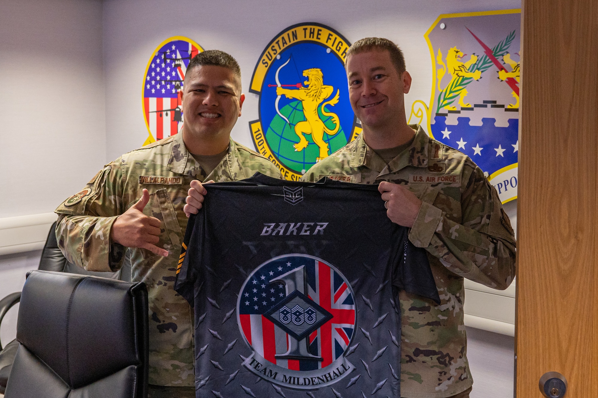 U.S. Air Force Master Sgt. Justin Villalpando, left, 100th Force Support Squadron first sergeant, and Chief Master Sgt. George Baker, right, U.S. Air Forces in Europe - Air Forces Africa command first sergeant, pose with a custom first sergeant jersey for Baker at Royal Air Force Mildenhall, England, Nov. 15, 2023.