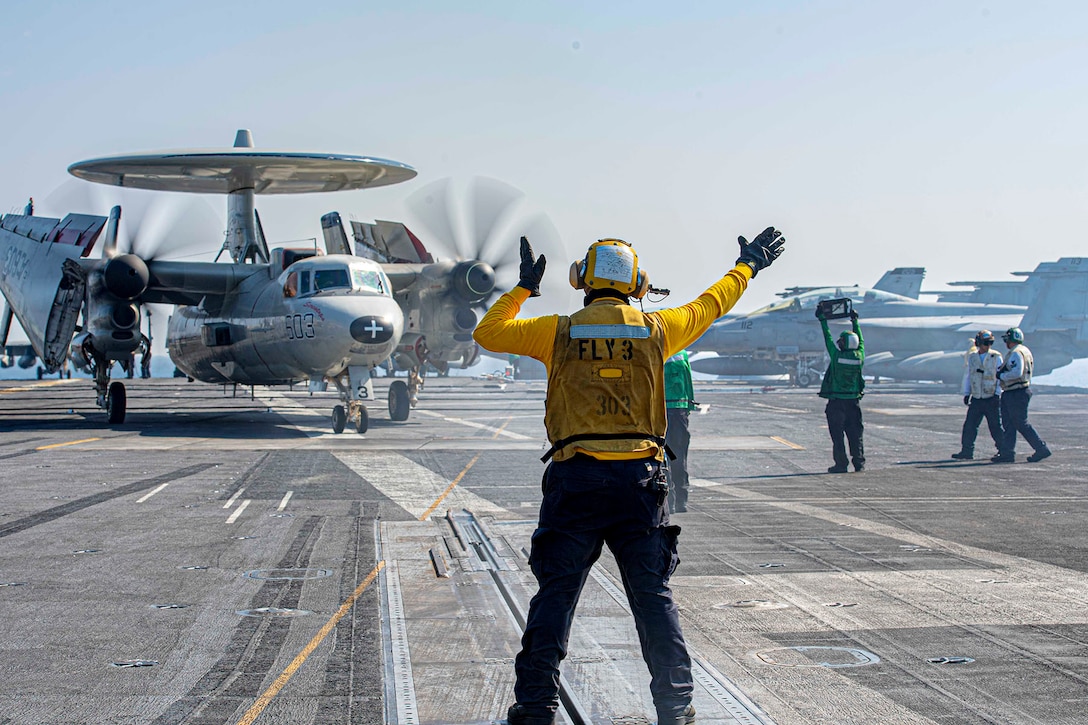A sailor gives directions to an E-2C Hawkeye on a flight deck.