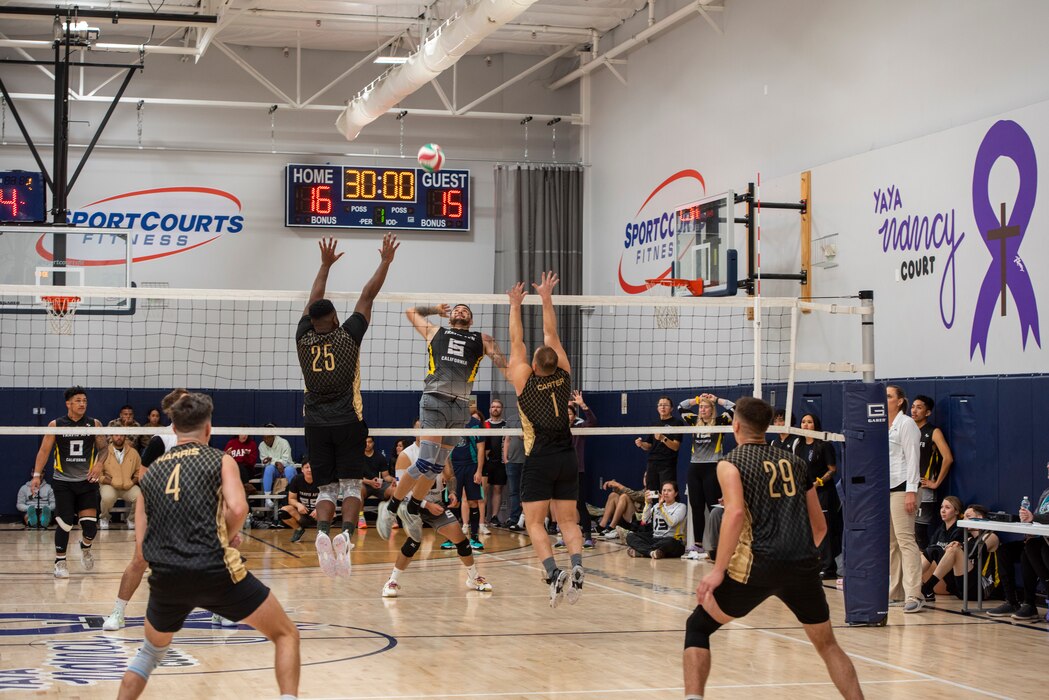 Volleyball players hit a ball over a net.