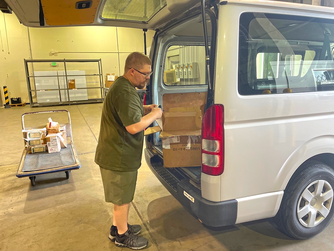 A man loads packages into the back of a van parked in a warehouse.