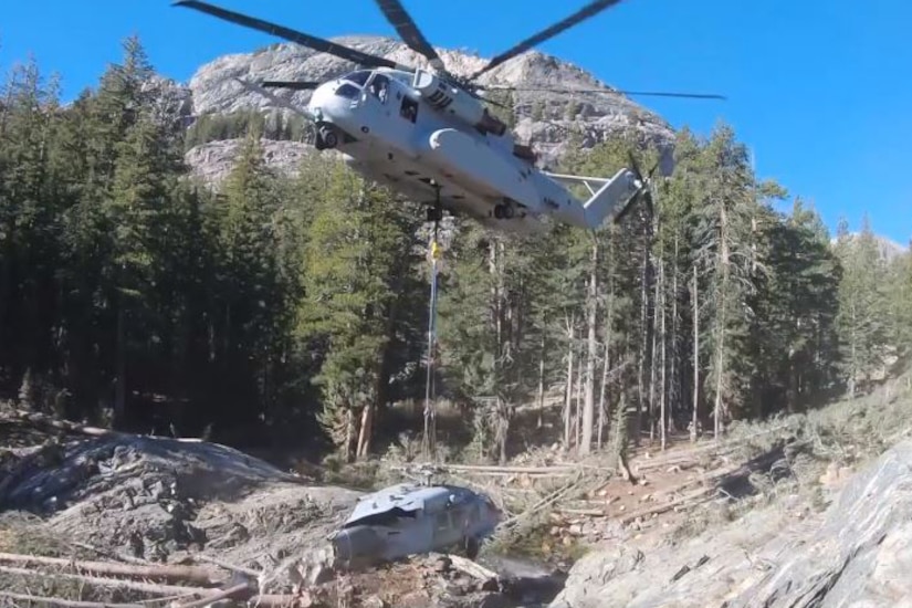 A helicopter lifts the remains of damaged helicopter.