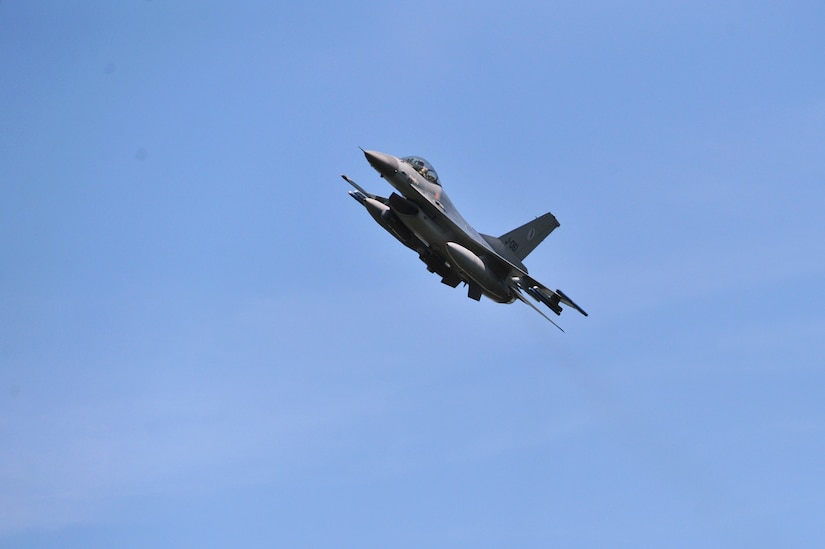A military aircraft flies against a blue sky.