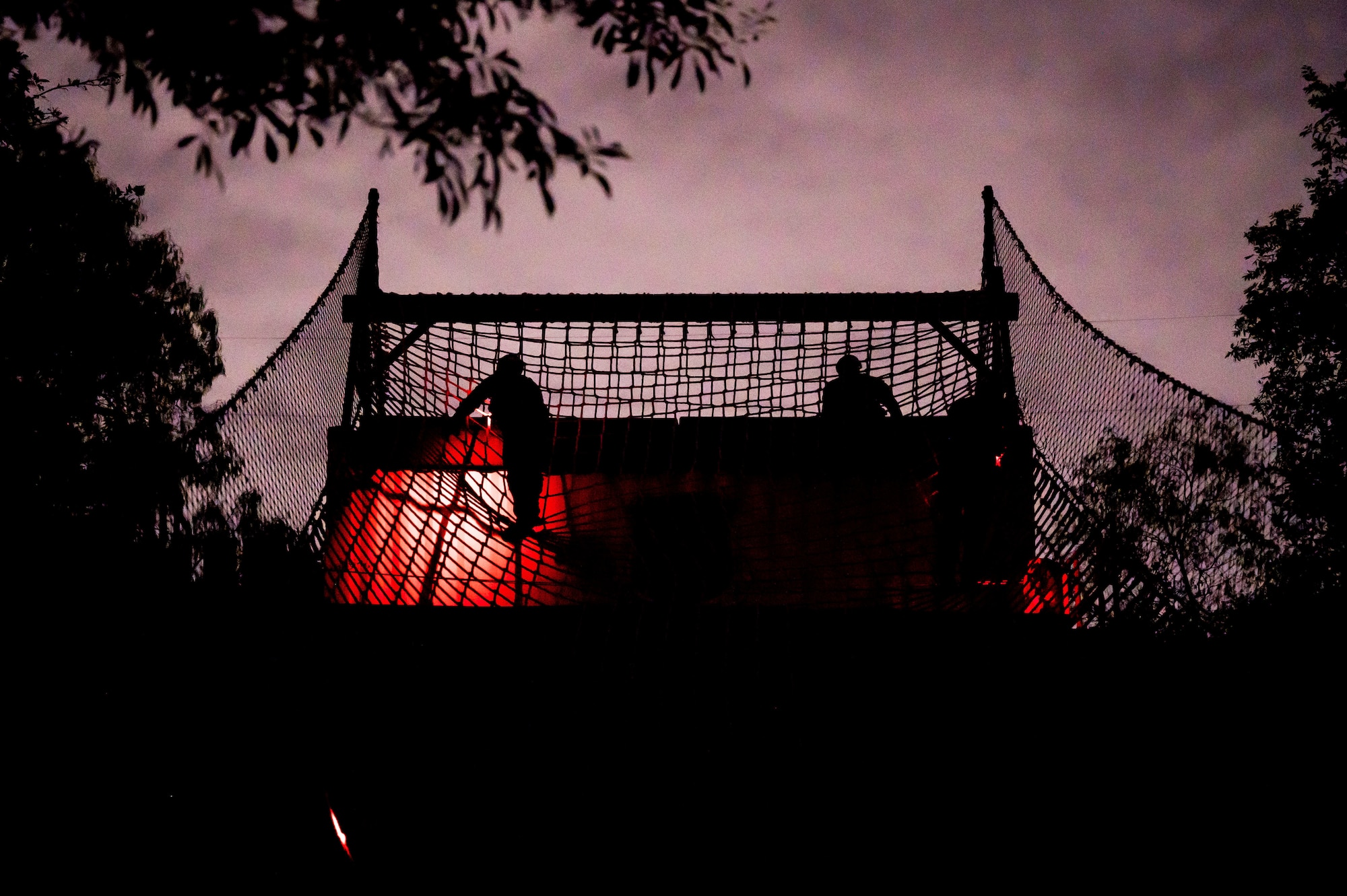 Silhouette climbs over rope bridge against the dark purple sky