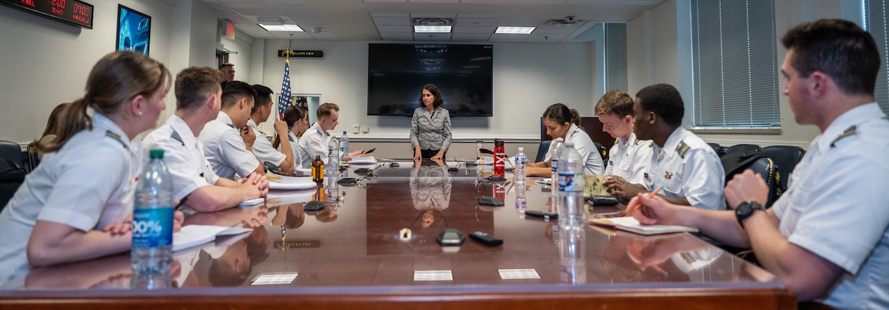 A woman speaks to cadets sitting around table in a conference room.