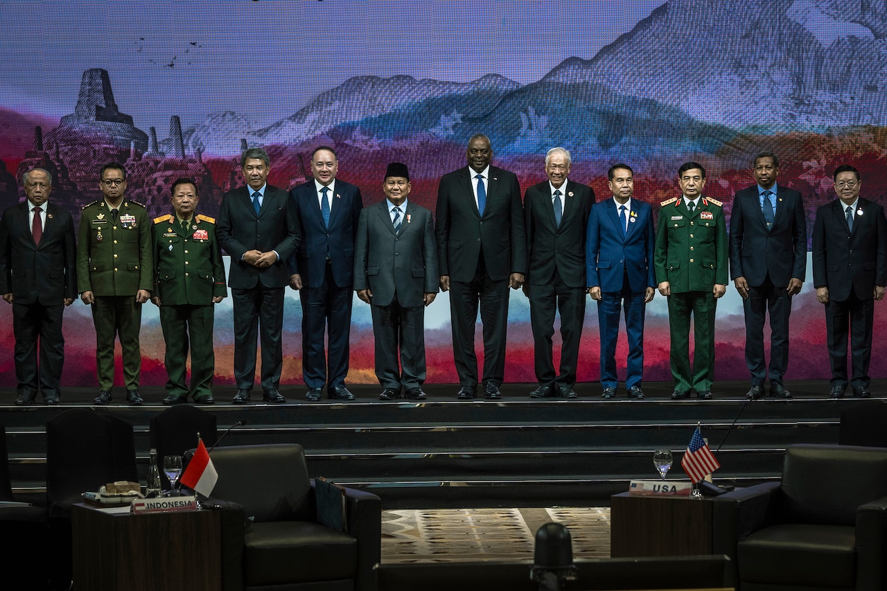 Secretary of Defense Lloyd J. Austin III is flanked by military and civilian leaders on a stage, five on his left, six on the right.