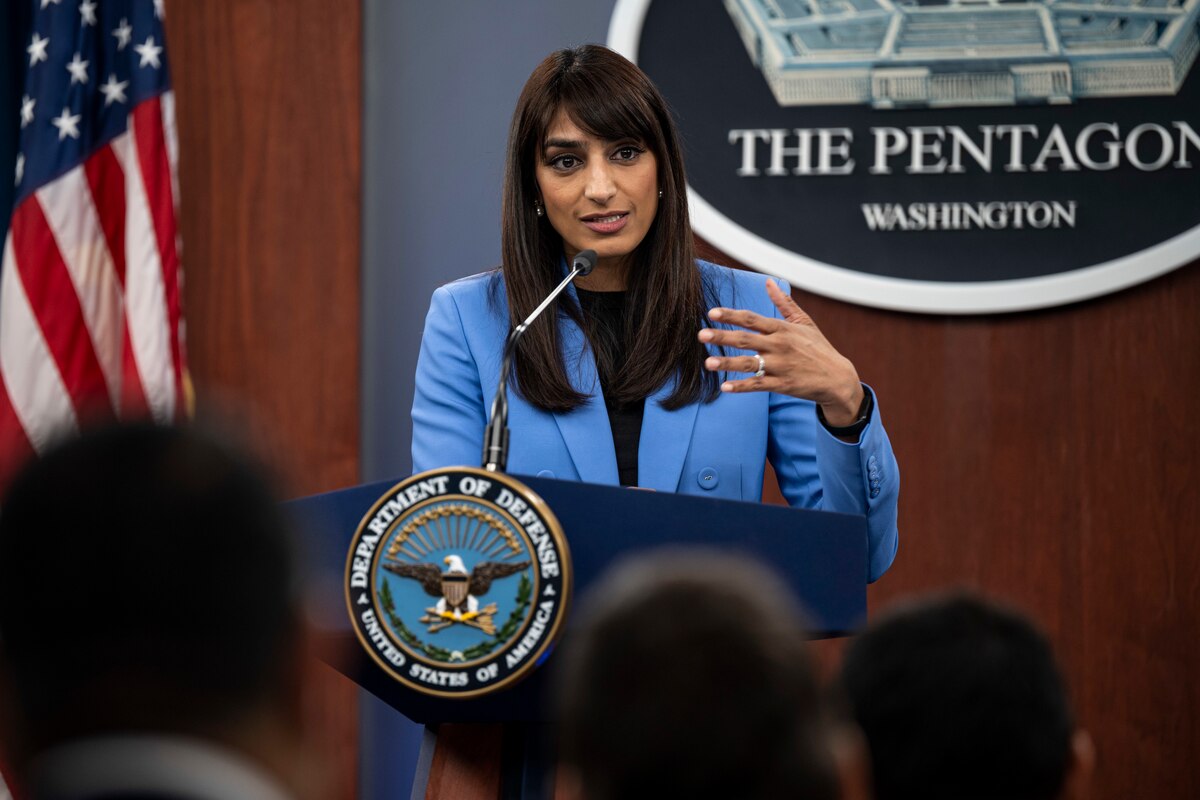 A woman stand behind a lectern. Behind her, a sign reads "the Pentagon."