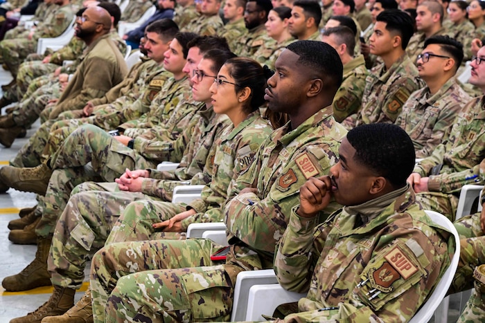 Airmen sit in the crowd and listen to a speaker at the all-call.