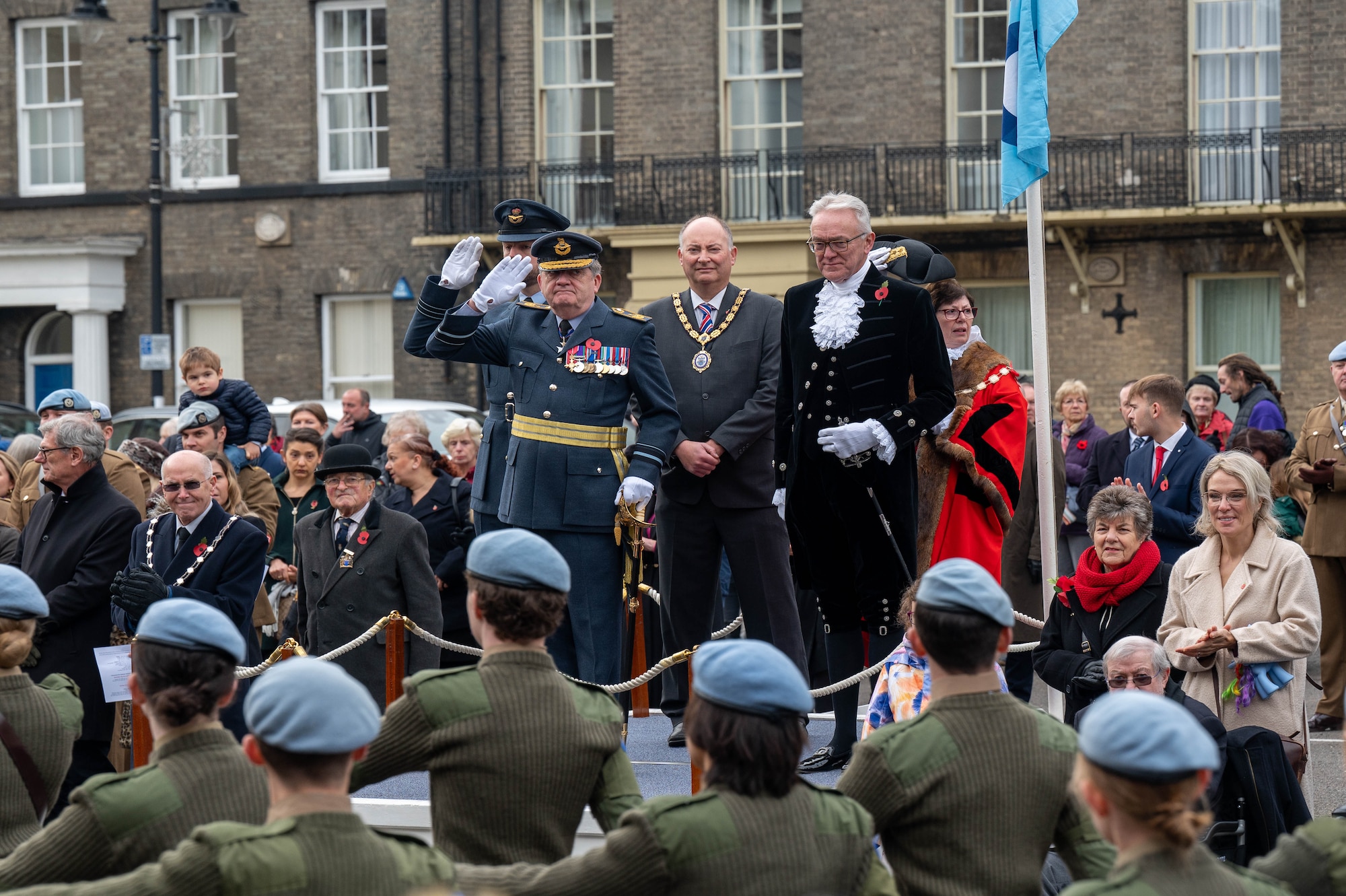 5 people stand on a stage watching a parade