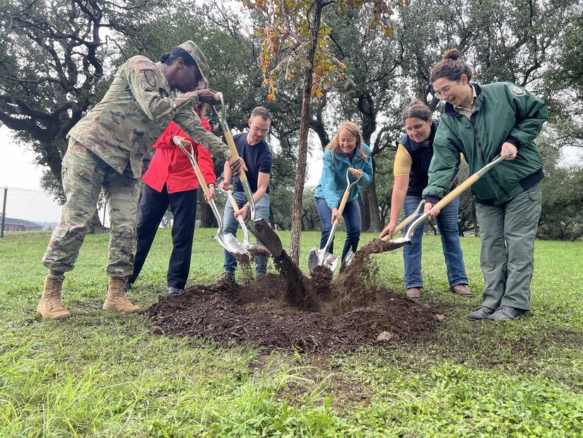A soldier and a group of people plant a tree.
