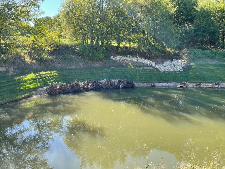 A creek is seen in the foreground with grass and trees in the background.