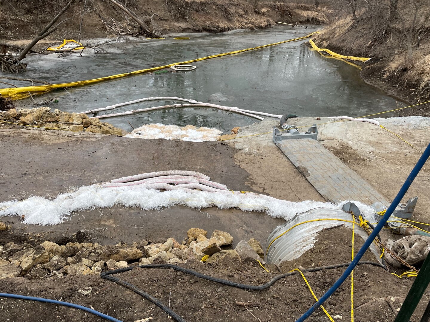 Black oil can be seen in a creek with a yellow caution tape in the left.
