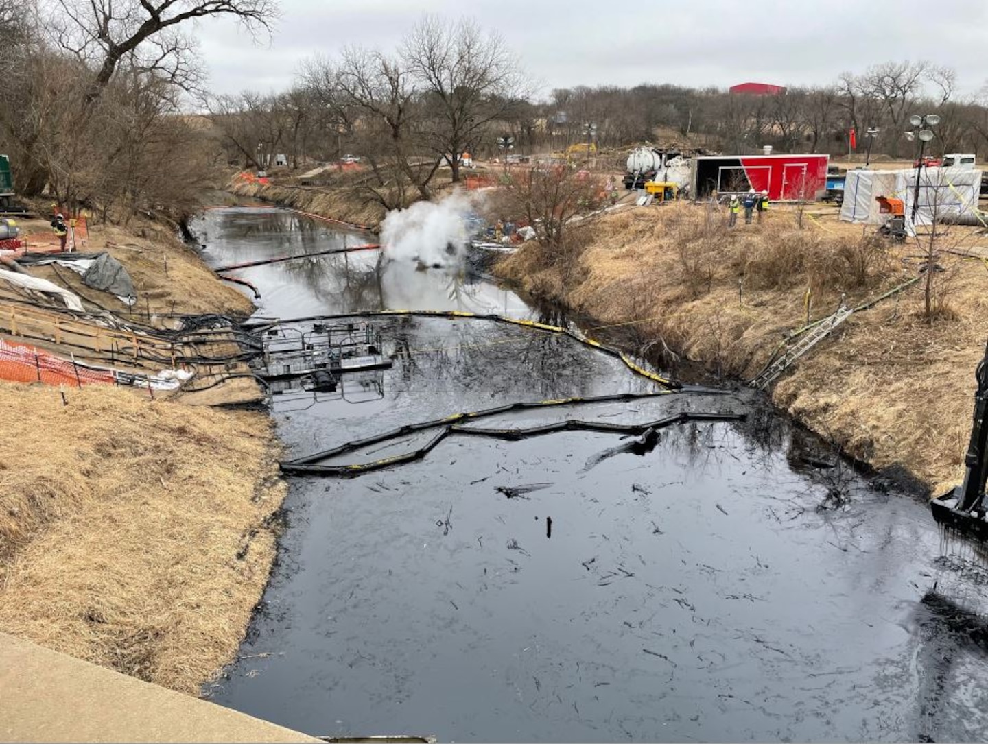 Black oil is seen in a stream between two stream banks with construction equipment to the right.