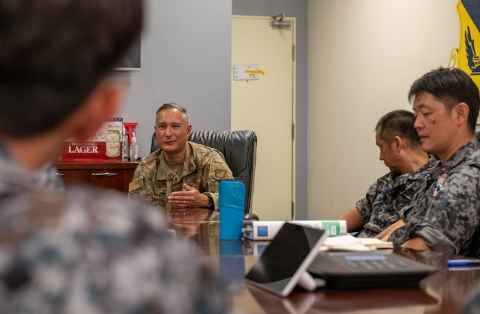 Four people in uniform sit around a desk and are talking in a room